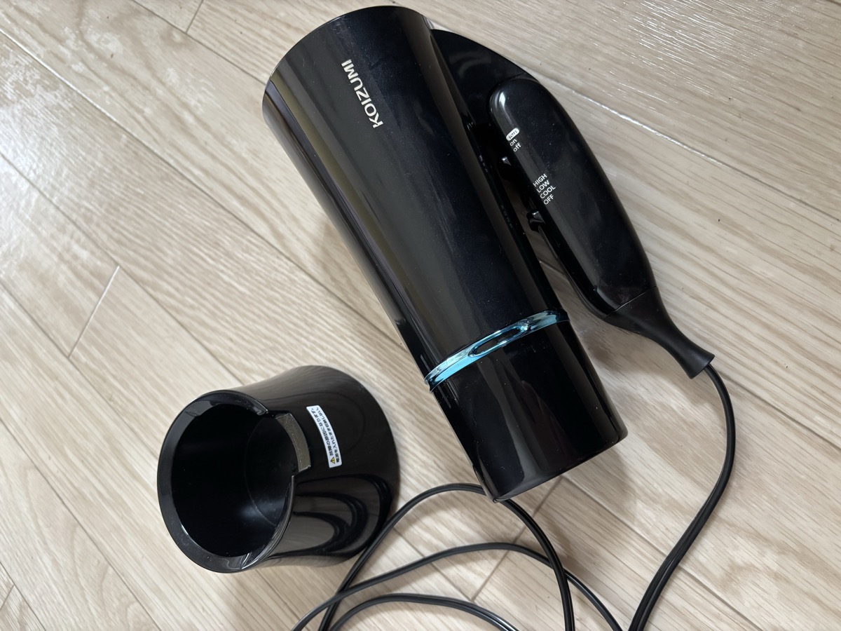 コイズミ コスメティックドライヤーKHD-K300本体と、コードを巻き付ける黒い専用スタンドを洗面所の床に並べたところ